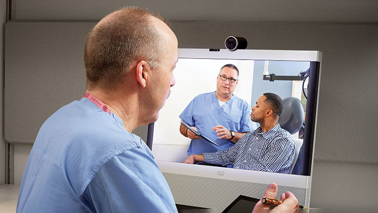 A doctor consults with another doctor and his patient via a virtual visit.